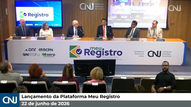 Uma imagem da transmissão ao vivo do evento "Lançamento da Plataforma Meu Registro", ocorrido em 22 de junho de 2026, promovido pelo Conselho Nacional de Justiça (CNJ). Ao fundo, seis autoridades estão sentadas em uma longa bancada branca que exibe o logotipo "meu Registro - Sistema Eletrônico dos Registros Públicos", acompanhado dos logos do CNJ e de outras entidades parceiras (ONR, ARCPN, IRTDPJ e SERP). À esquerda e à direita da bancada, telas exibem a marca do evento. Em primeiro plano, vê-se a parte de trás da cabeça de algumas pessoas na plateia e, no canto inferior direito, um intérprete de Libras. Uma barra informativa azul e cinza na parte inferior da tela exibe o logotipo do CNJ e o título do evento com a data.